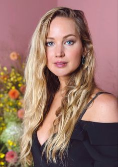 a woman with long blonde hair and blue eyes posing in front of a pink wall