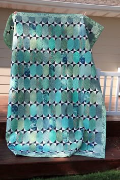 a blue and green quilt sitting on top of a wooden bench in front of a house