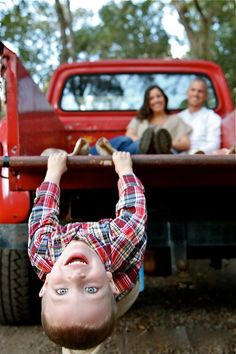 a young boy hanging upside down in the back of a red truck