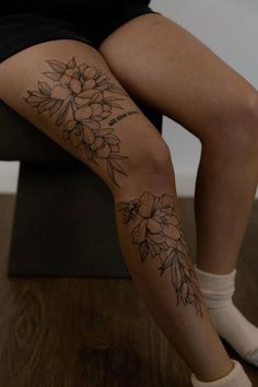 a woman sitting on top of a wooden bench with flowers tattooed on her leg and legs