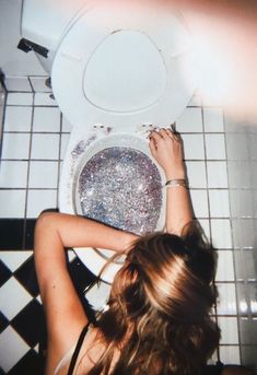 a woman is sitting in front of a toilet with glitter on the seat and lid