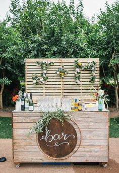 an outdoor bar with bottles and glasses on it, surrounded by greenery in the background