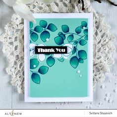 a thank you card with white flowers and green leaves on a lace doily next to a crochet doily