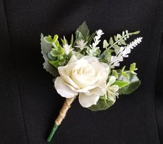 a boutonniere with white flowers and greenery on the lapel pin