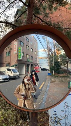 a woman standing in front of a mirror on the side of a road next to a tree