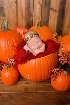 a baby is sleeping in a pumpkin basket surrounded by fall leaves and other autumn decorations