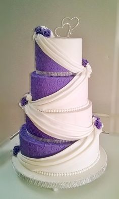 a purple and white wedding cake with hearts on top