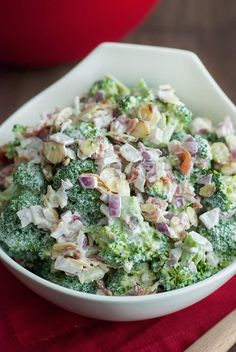 a white bowl filled with broccoli salad on top of a red cloth