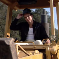 a man sitting in the driver's seat of a yellow bulldozer with trees in the background