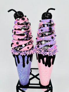 two cupcakes with black and pink frosting on them, one is covered in sprinkles