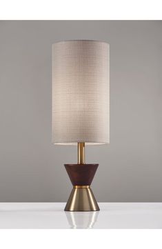 a table lamp with a white shade on it and a wooden base in front of a gray wall