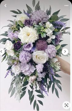 a purple and white bouquet with greenery on the bottom is being held by someone's hand