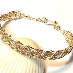 a close up of a gold bracelet on a white surface with a shell in the background