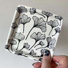 a hand holding a black and white flowered square plate with flowers on it's sides