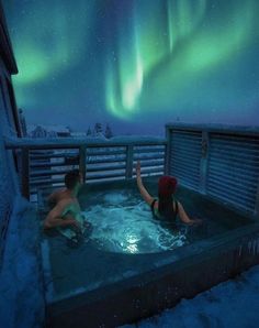 two people in a hot tub with the northern lights behind them