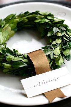 a white plate topped with a green wreath on top of a wooden table next to a name tag