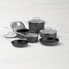 an assortment of pots and pans on a marble countertop, with one empty skillet in the middle