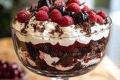 a dessert with chocolate, raspberries and whipped cream in a glass dish on a wooden table