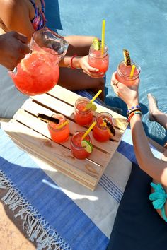 people are sitting by the pool with drinks in their hands