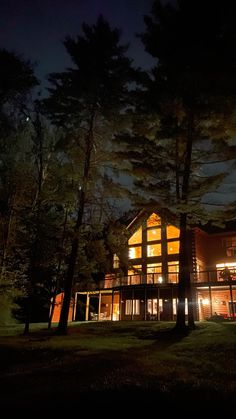 a large house lit up at night in the woods with lights on it's windows