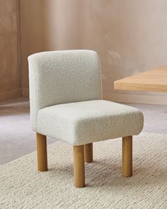 a white chair sitting on top of a rug next to a wooden table and wall