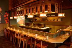 the interior of a japanese restaurant with wooden tables and chairs, lights hanging from the ceiling