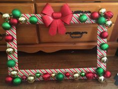 a christmas photo frame with ornaments and a bow on it's front end, sitting in front of a dresser