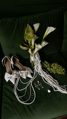 a pair of white shoes sitting on top of a green couch next to pearls and flowers