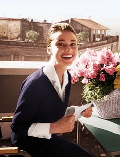 a woman sitting at a table with flowers in front of her and holding a piece of paper