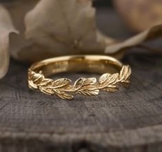 a gold wedding band with leaves on it sitting on top of a piece of wood