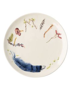 a white plate with blue feathers and flowers painted on the side, in front of a white background