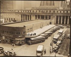 an old black and white photo of buses parked in front of a building with people walking around