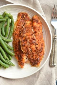 a white plate topped with meat and green beans next to a fork on a table