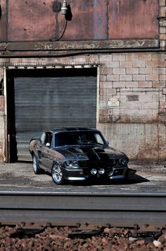 a black car parked in front of a brick building next to train tracks and a street light