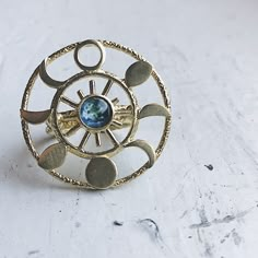 "What a knockout! This textured raw brass gold tone ring is set with the Earth in glass surrounded by 8 different phases of the moon in a round halo. Celebrate the cosmos and our planetary home with this piece of galaxy jewelry! Ring Size: Adjustable Design Size: 1 1/4\" (3.2cm) Materials: Raw brass, glass ★ These are individually handcrafted and the particular piece you receive may vary slightly from what is pictured. These are also not 100% waterproof, so please avoid submerging them in water. Luxury Silver Celestial Crystal Ring, Luxury Moon Phase Rings For Anniversary, Luxury Celestial Crescent Ring, Circle The Fifths Ring, Luxury Moon Phase Ring Jewelry, Moon Ring Color Chart, Halo Ring Planet, Luxury Blue Celestial Rings, Luxury Celestial Crystal Gemstone Ring