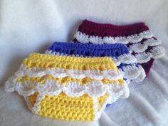 three crocheted panties are laying on a white sheet and one is yellow, the other is red