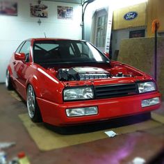 a red car parked in a garage with its hood up and the engine bay open