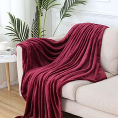 a white couch with a red blanket on top of it next to a potted plant