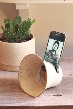 a cell phone sitting in a cup on top of a wooden table next to a plant