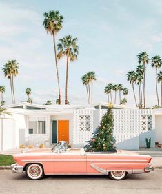 an old pink car parked in front of a house with a christmas tree on top