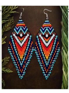 a pair of colorful beaded earrings sitting on top of a table next to pine branches