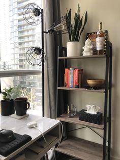 a room with a desk, bookshelf and other items on the shelves in front of a window