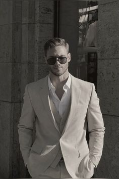 a man in a white suit and sunglasses posing for a black and white photo with his hands in his pockets