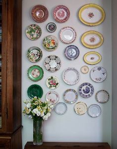 a vase filled with flowers sitting on top of a wooden table next to a wall covered in plates