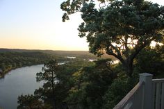 the sun is setting over a lake and trees in the foreground, with a wooden fence to the right