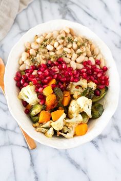 a bowl filled with beans, cauliflower and broccoli on top of a marble counter