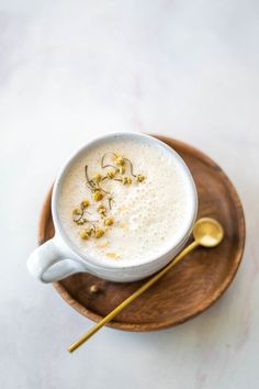 a cup of coffee with some flowers in it on a wooden plate next to a spoon