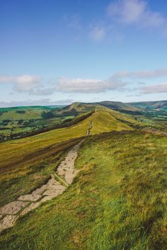 a grassy hill with a path leading to the top and green hills in the distance