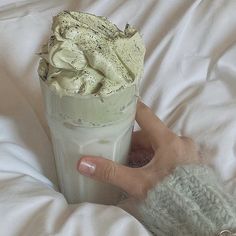 a hand holding a drink with whipped cream in it on top of a white blanket