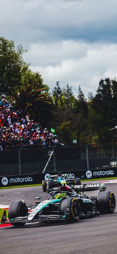 two racing cars driving on a race track with people watching from the stands behind them